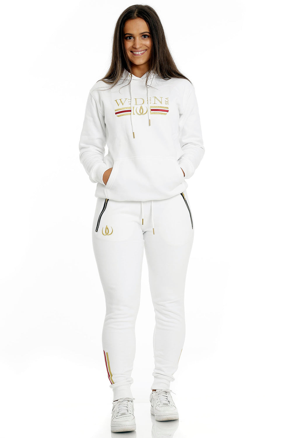 Standing in white joggers with gold logo and a white hoodie with gold embroidery, worn with white sneakers.