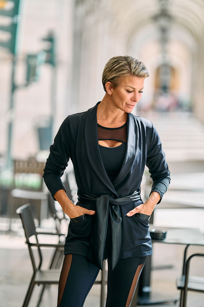 Sotto un porticato con le mani nelle tasche del blazer. La canotta sotto ha un inserto in mesh sul petto.