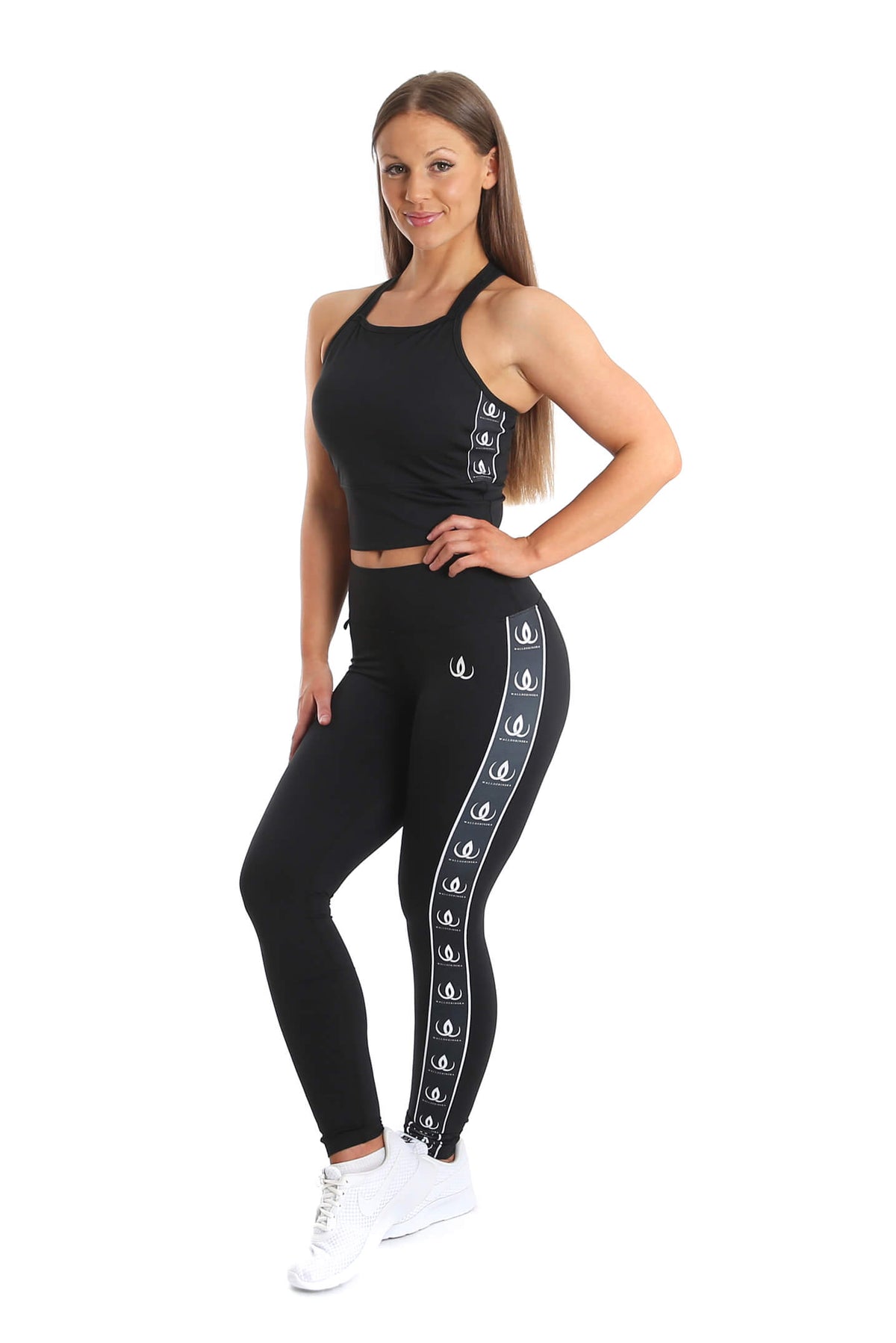 Crop top e leggings neri con fasce bianche con logo lungo il lato, completati da sneakers bianche.