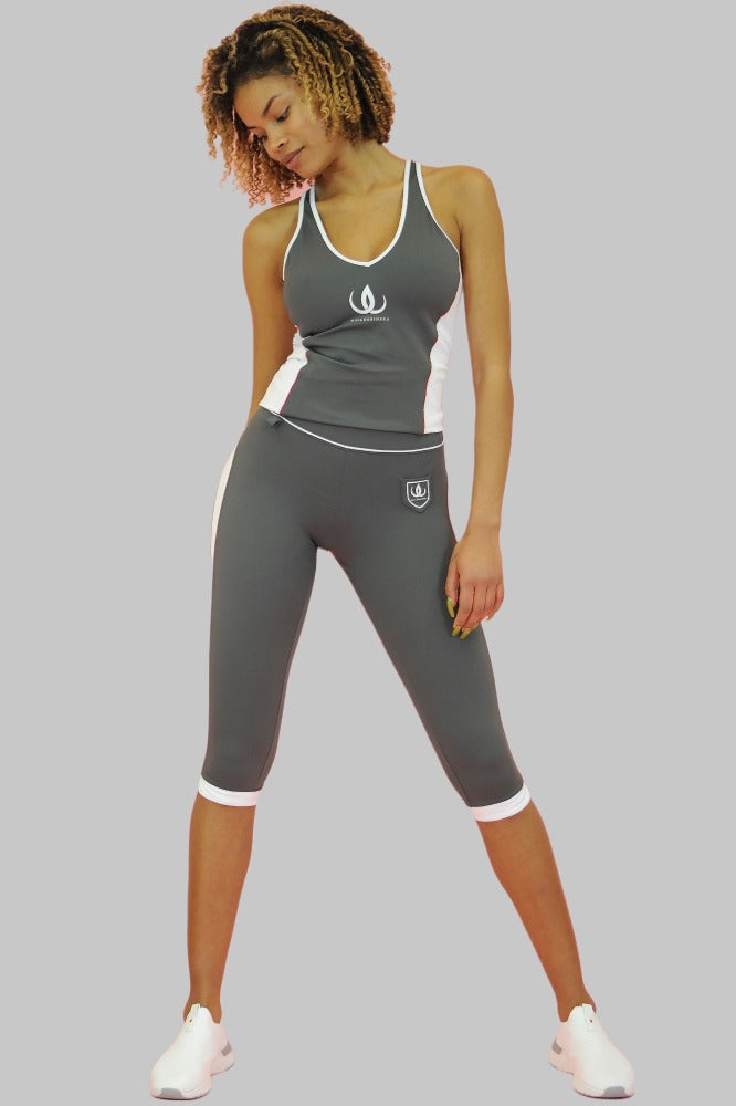 I leggings capri grigi hanno un logo bianco a scudo sulla coscia e bordi bianchi in fondo. La modella indossa una canotta grigia.