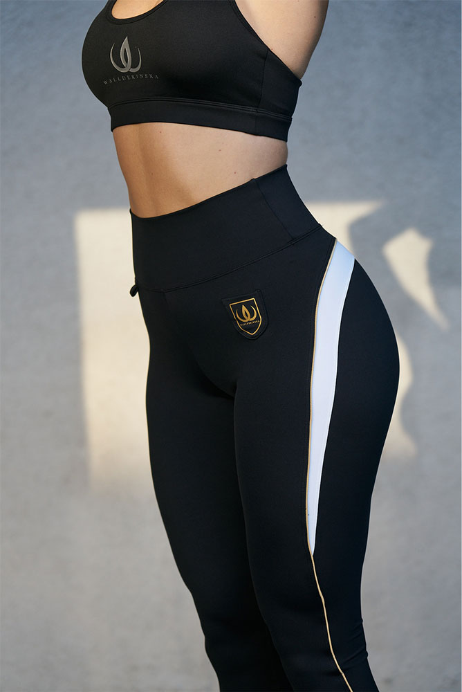 I leggings neri hanno il logo oro sul fianco e una riga bianca bordata d'oro lungo il lato.