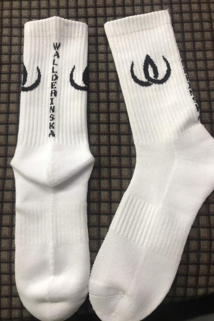 A pair of white socks with a black logo and emblem along the leg, against a dark background.
