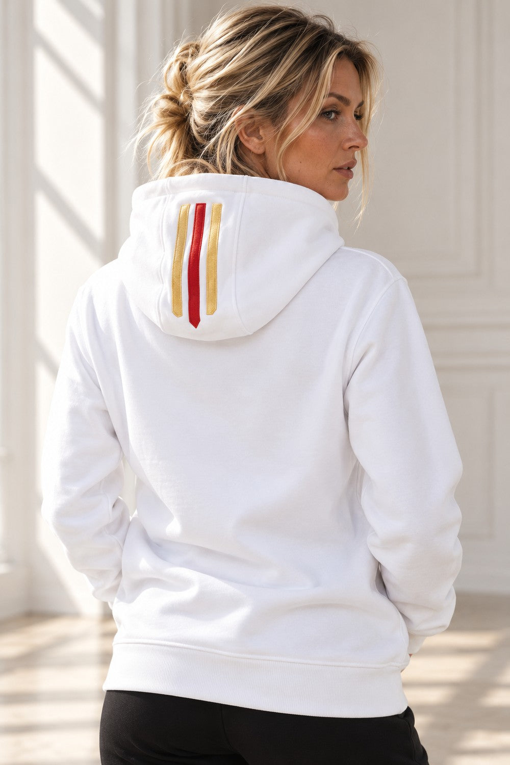 Rött och guldfärgat streck längs huvan på den vita Deluxe Hoodie, sedd bakifrån.