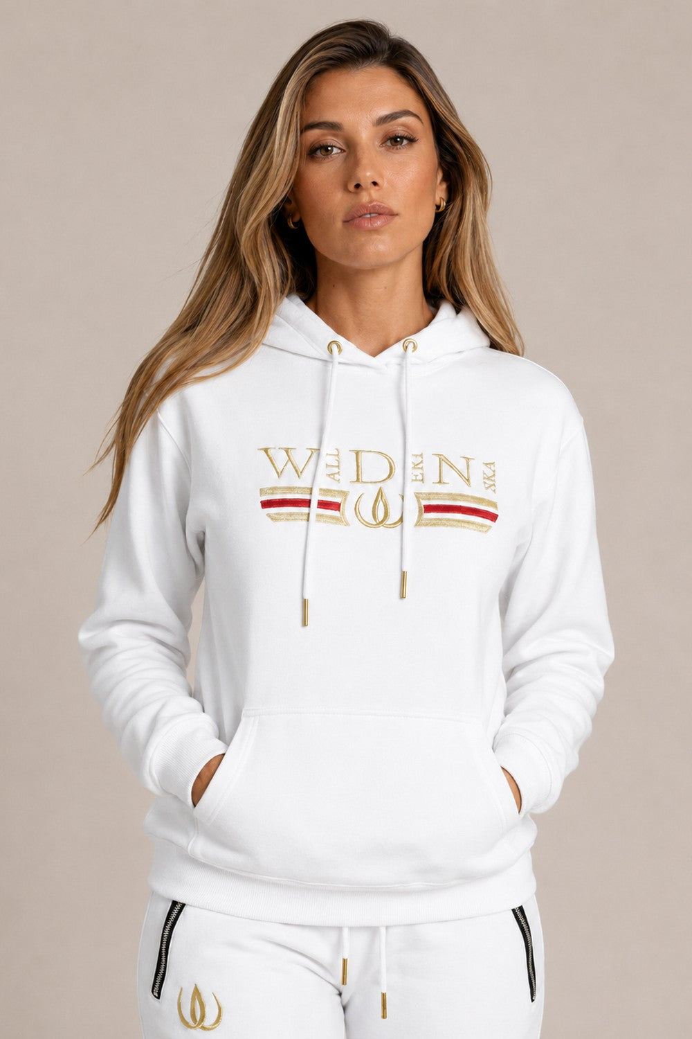 White Deluxe Hoodie with gold embroidery and a red stripe across the chest, worn with white Deluxe Joggers with a gold logo.