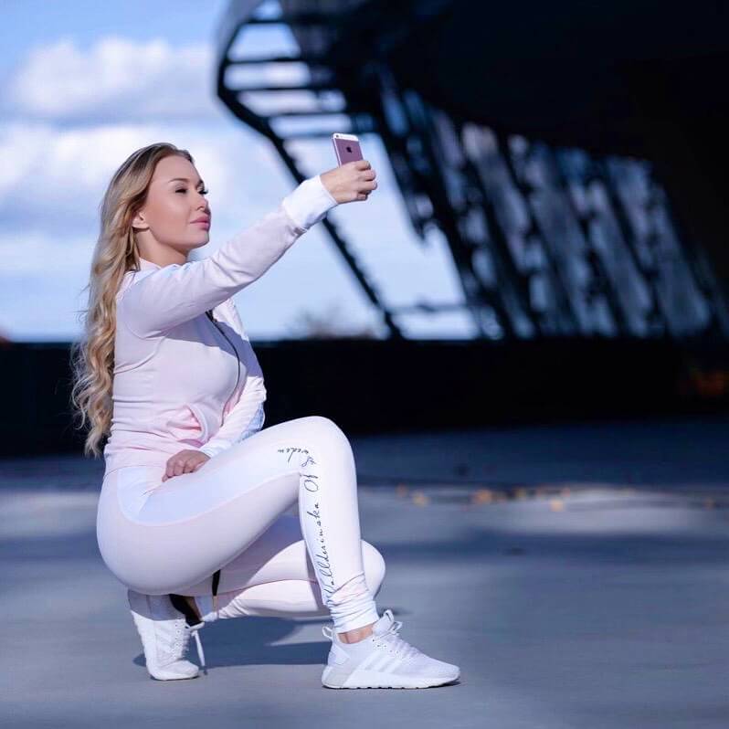 Utomhus på ett tak sitter modellen på huk i de ljusrosa träningsbyxorna och matchande jacka.