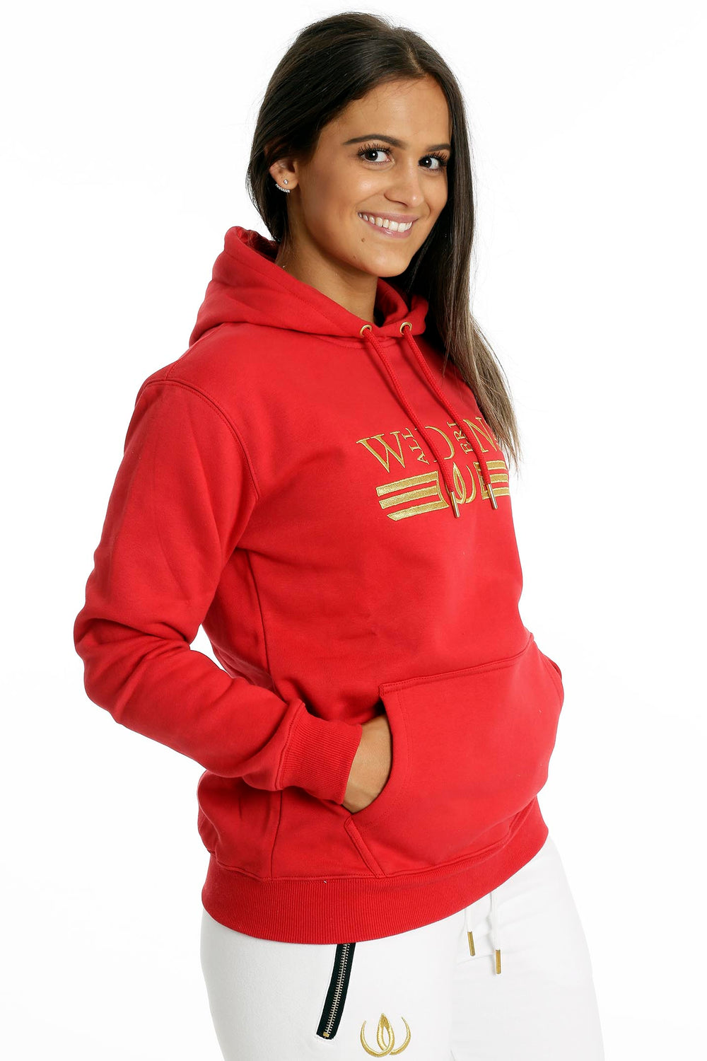 The hands rest in the kangaroo pocket of the red hoodie. Below are white joggers with a gold-toned zip.