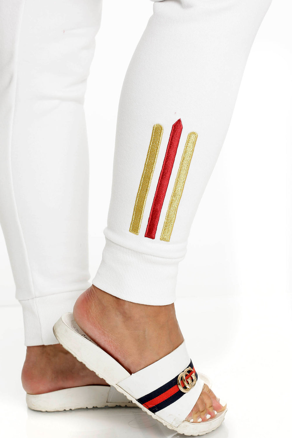 At the ankle of the white trousers sit two gold stripes and one red, above a ribbed cuff.