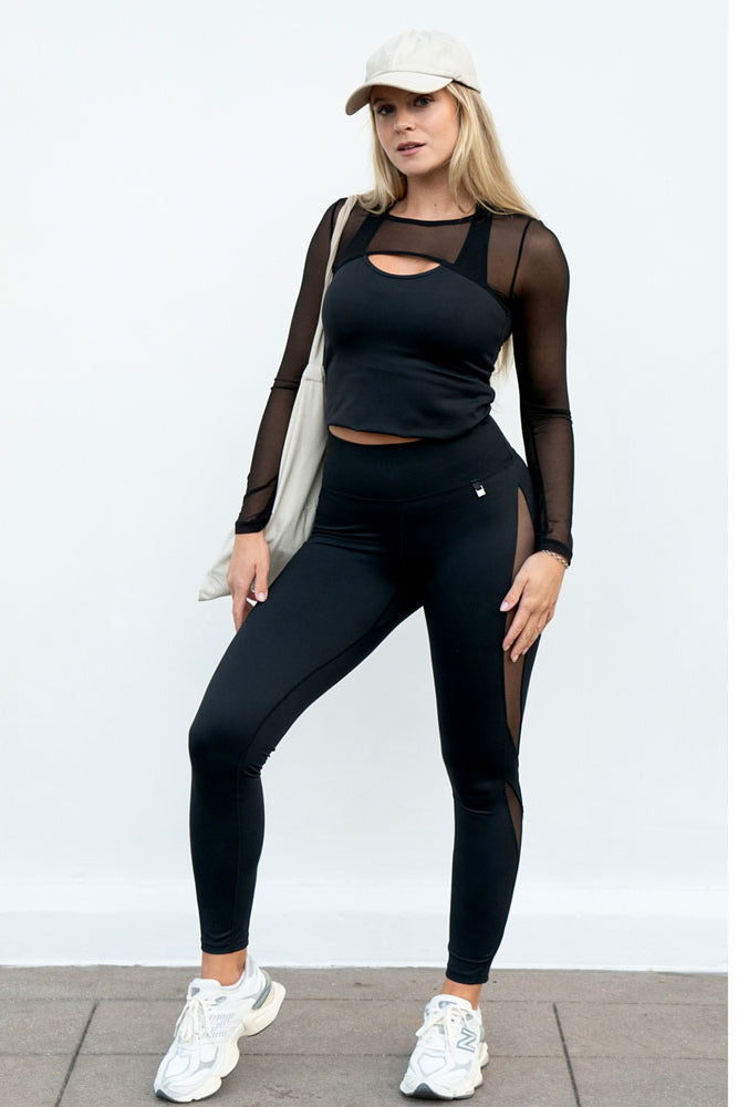 A black top with mesh sleeves, a cap and a white tote bag are worn with the leggings.