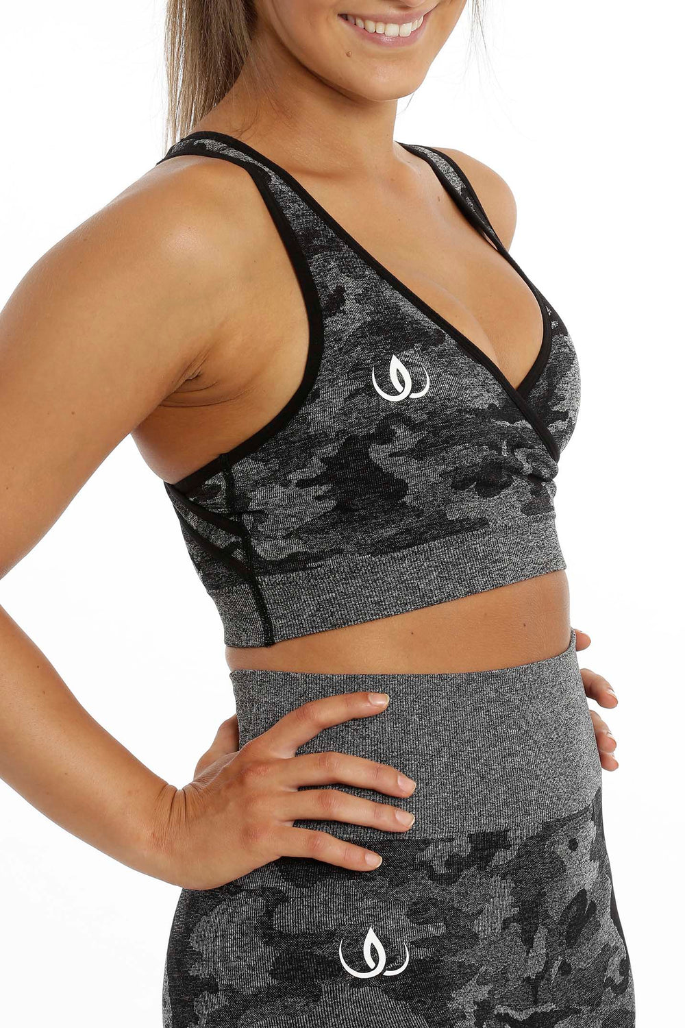 The top seen at an angle from the side with a white logo on the chest, above leggings in the same camouflage.