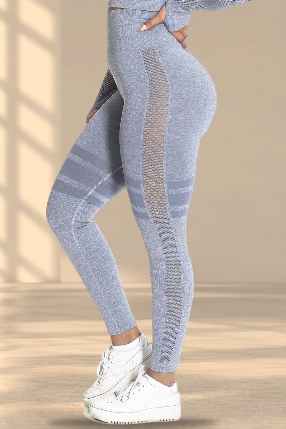 De zijkant van de grijze legging met meshinzet en gestreepte banden, boven witte sneakers.