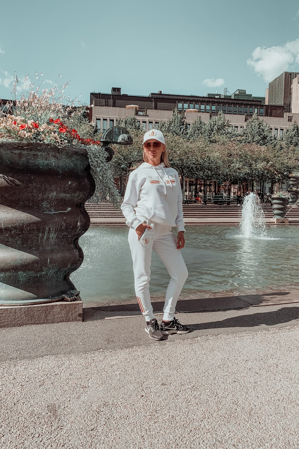In front of the fountain the model stands in a white hoodie, white joggers and a white cap.