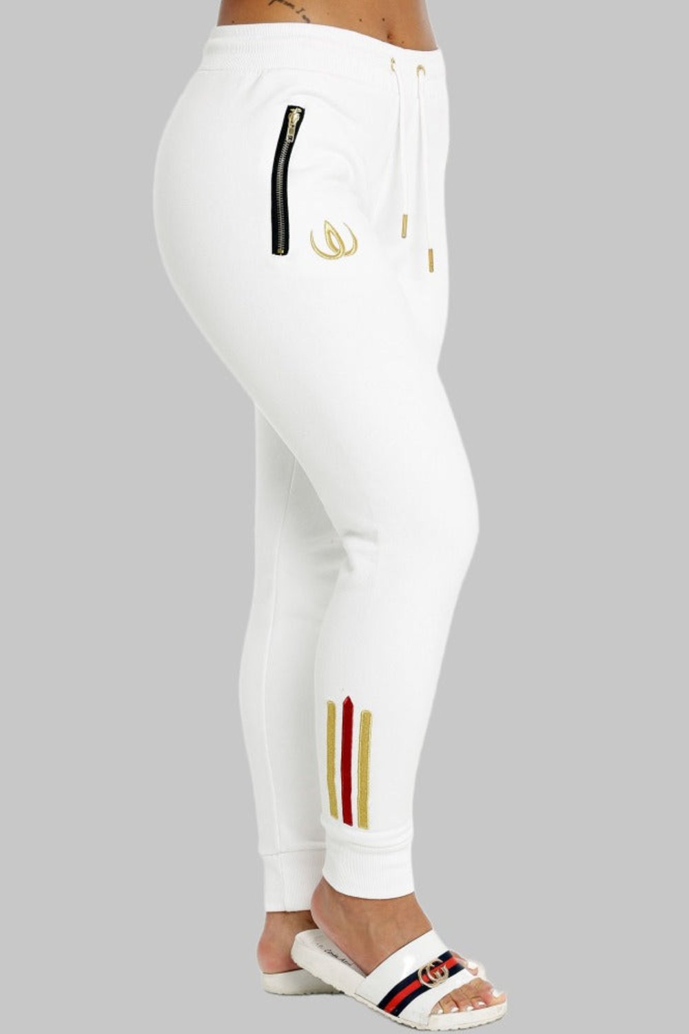 White joggers in profile with a gold-toned zip on the pocket, a gold logo on the thigh and stripes at the ankle.