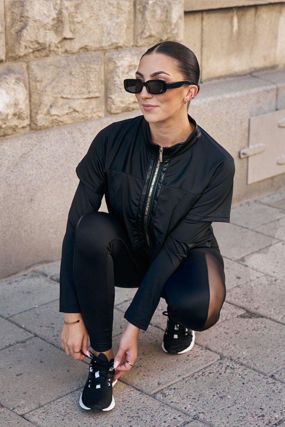 At the kerb the model crouches to tie her shoe, in the black jacket and black leggings.