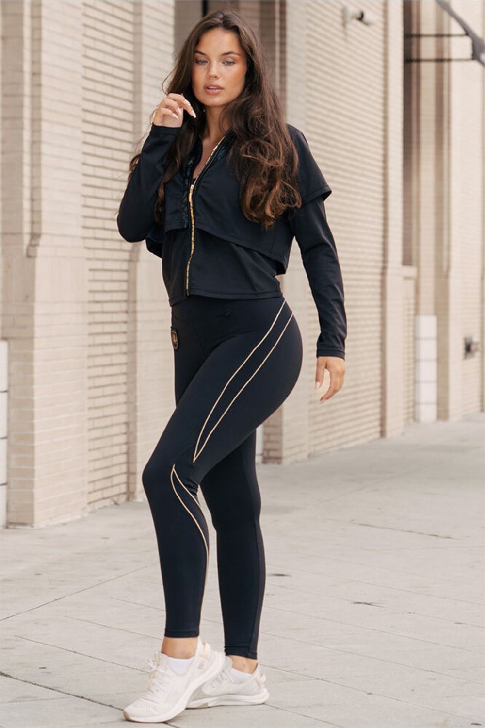 In front of the brick wall, the model stands in the jacket and black leggings with gold lines.