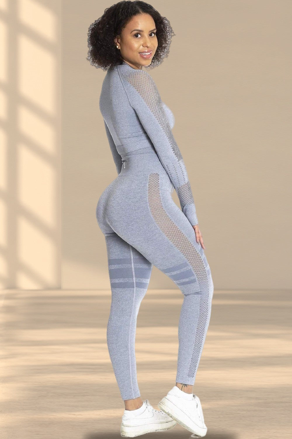 Het model kijkt over de schouder in een grijze legging en bijpassende trui, met witte sneakers.